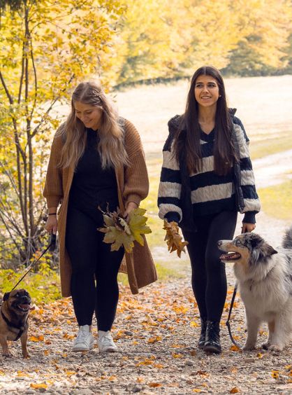 Zwei Frauen gehen im Wald mit zwei Hunden spazieren