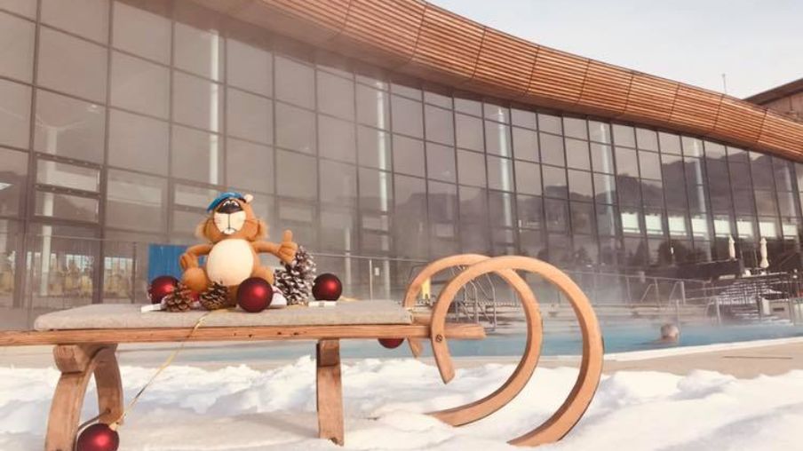 Schlitten im Schnee mit Therme im Hintergrund