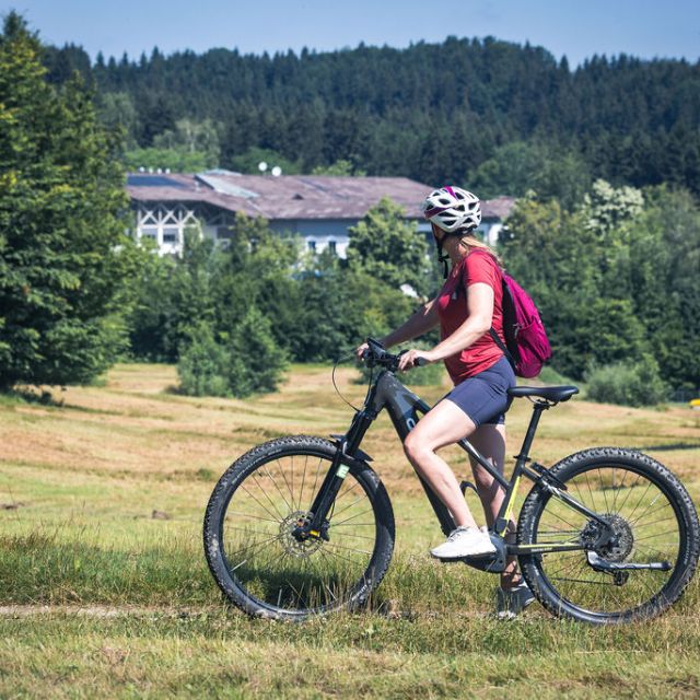 Frau sitzt am Fahrrad und schaut auf den Aldiana Club Ampflwang 