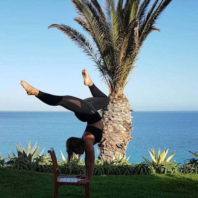 Frau macht einen Handstand auf der Wiese mit Meer im Hintergrund