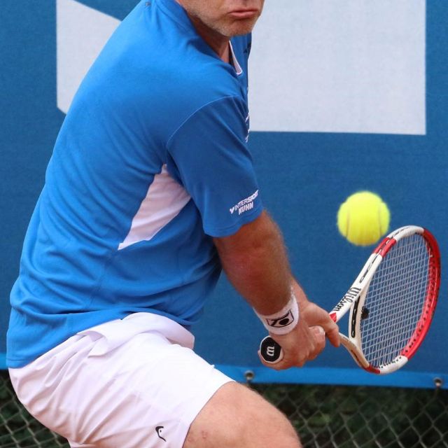 Tennisspieler schaut angespannt und schießt mit Schläger Tennisball weg 