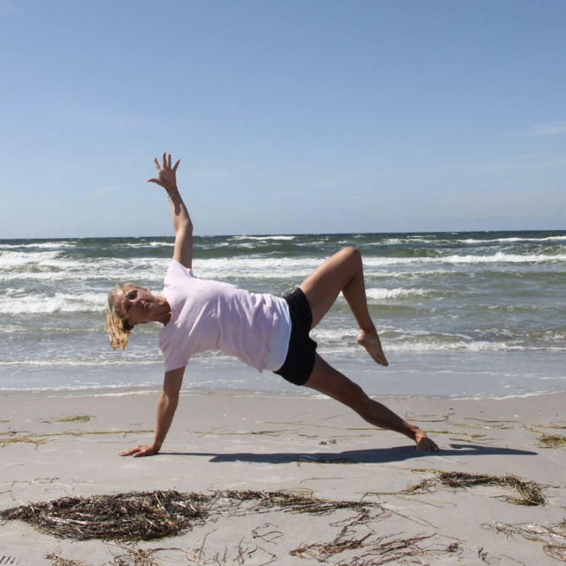 Frau macht Yoga am Strand mit Meer im Hintergrund