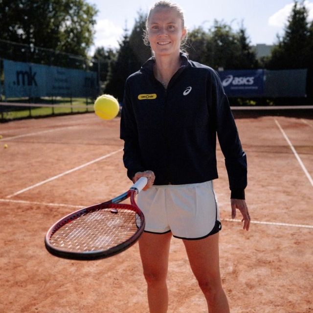 Frau steht auf den Tennisplatz und wirft einen Tennisball mit einem Schläger in die Luft