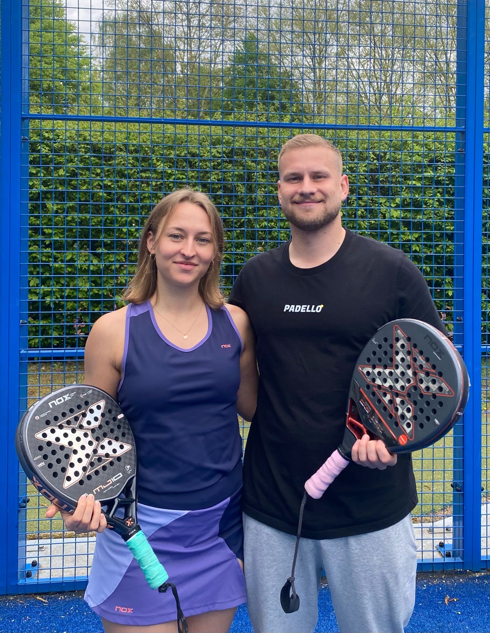 Zwei Personen lächeln in die Kamera mit Padel Schläger